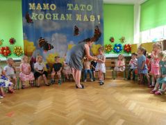 dzieci siedzą na krzesełkach recytują, pani rozdaje rekwizyty