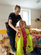 Pani policjantka pokazuje dzieciom kamizelkę odblaskową