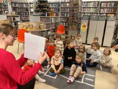 Dzieci siedzą na dywanie w bibliotece, pani czyta.