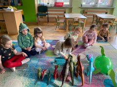 Dzieci siedzą na dywanie oglądają zabawki dinozaury