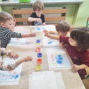 Dzieci wykonują pracę plastyczną przy stolikach