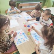 Dzieci wykonują pracę plastyczną przy stolikach