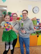 Dziewczynka z kolorową pisanką pozuje do zdjęcia z rodzicami