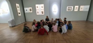 Dzieci uważnie słuchają siedząc na podłodze.