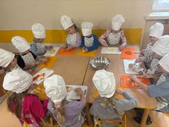 Dzieci wspólnie wykonują sałatkę w strojach kucharzy.