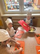 Dzieci wspólnie wykonują sałatkę w strojach kucharzy.