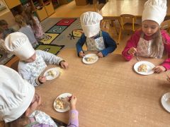 Dzieci wspólnie degustują sałatkę w strojach kucharzy.