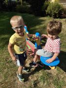 Jeden chłopiec siedzi na bujaku, drugi stoi obok niego.