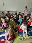 Dzieci w bibliotece siedzą na dywanie słuchają opowiadania. Pani czyta.