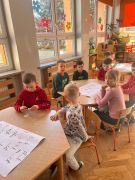 Dzieci siedzą przy stolikach podczas zajęć z literkami.