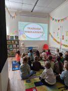 Dzieci w bibliotece na dywanie słuchają prezentacji na temat zwyczajów wielkanocnych.